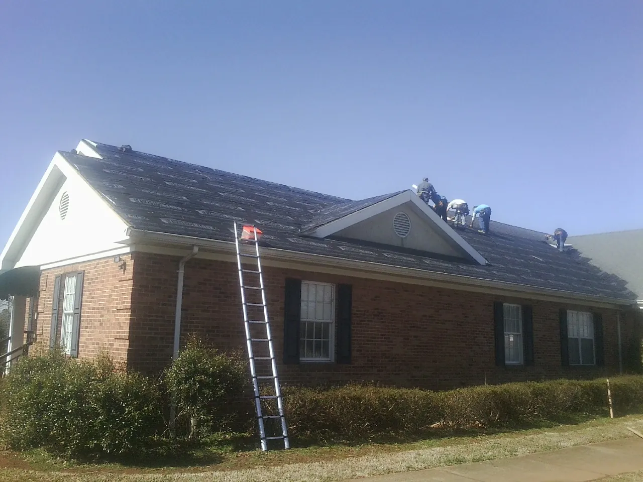 Crew tearing shingles off a brick ranch roof with a ladder set — Emergency Roof Repair work by our crew in Tygh Valley