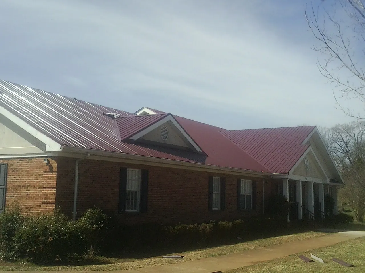 Red metal roof with gabled entries on a long brick building, from a Hail Damage Roof Repair job in Tygh Valley