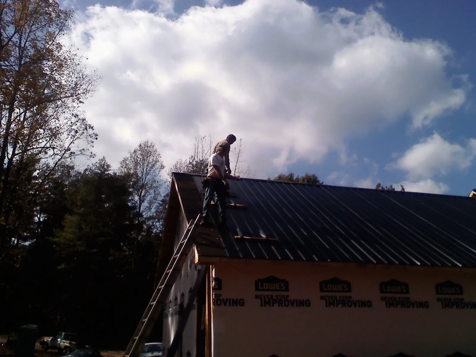 Roofer fastening dark metal panels high against a cloudy sky, from a Roof Inspection job in Tygh Valley